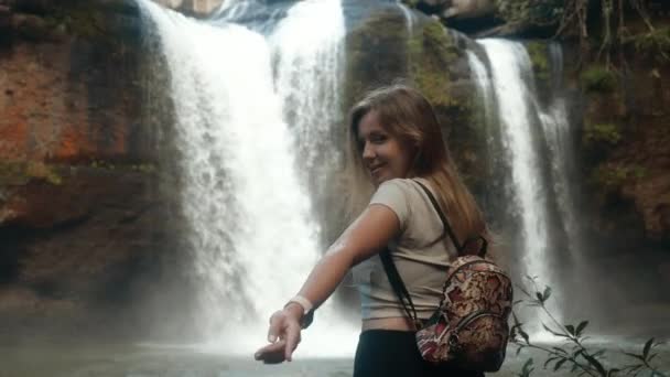 Attraente spensierata giovane donna vicino alla cascata si gira e invita a unirsi — Video Stock