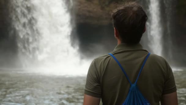 Vista trasera del mochilero hombre de viaje en la cascada, disfrutar de la naturaleza y la selva tropical — Vídeo de stock
