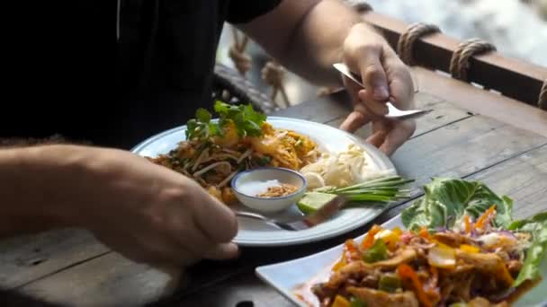 Παραδοσιακό ταϊλανδέζικο - pad thai. Ο άνθρωπος τρώει φρέσκα τρόφιμα κοντά καταρράκτη στο καφέ — Αρχείο Βίντεο