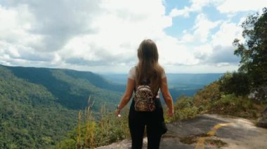 Sırt çantasıyla dağ zirvesinde gezen genç bir kadın yürüyüşçü manzarası ile ayakta duruyor.