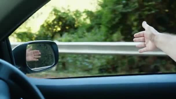 Вільний чоловік, який подорожує на машині, ловить вітер з рукою з вікна автомобіля — стокове відео