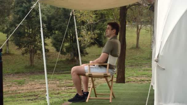 Człowiek odpocząć i cieszyć się przyrodą, siedzi w pobliżu nowoczesnego namiotu namiotu turystycznego — Wideo stockowe