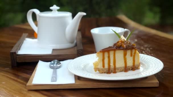 Pedazo de delicioso pastel fresco en la mesa de madera con tetera blanca en la cafetería al aire libre — Vídeo de stock