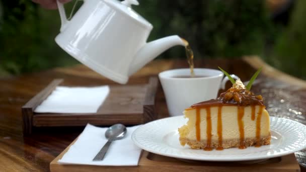 Mano de hombre vertiendo té caliente en taza de té. Pedazo de delicioso pastel fresco en la cafetería — Vídeos de Stock