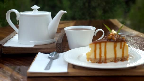 Шматок смачного свіжого торта на дерев'яному столі з білим чайником у відкритому кафе — стокове відео