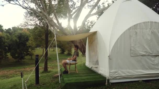 Traveler man enjoying nature, sitting on chair near canvas modern camp tent — Vídeo de Stock