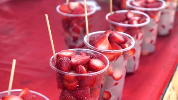 Fresas cortadas y peladas en tazas de plástico con palos de madera para comer — Vídeo de stock