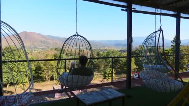 Neobvyklá kavárna s visícími židlemi a výhledem na zelené hory a modré nebe — Stock video