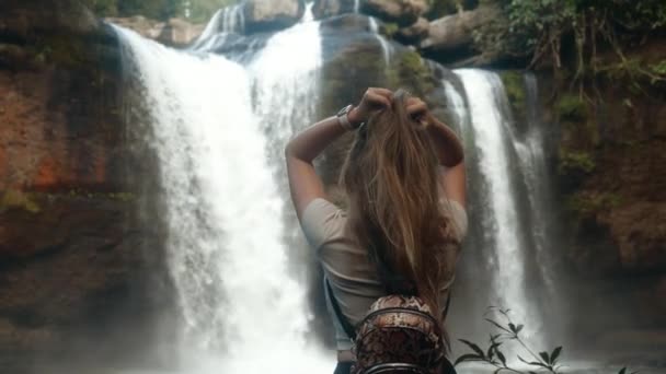 Sensuale donna si sta godendo la natura sulla cascata nella giungla, tocca i suoi lunghi capelli — Video Stock