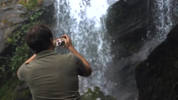 在黑暗的热带雨林里带着手机拍摄瀑布的旅行男子 — 图库视频影像
