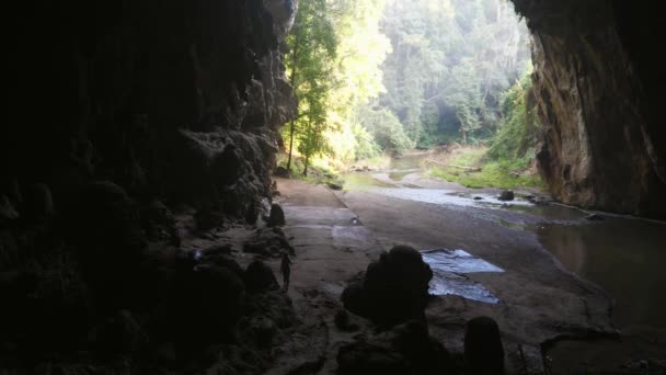 Γυναικεία σιλουέτα περπατά μέσα από σκοτεινή σπηλιά στην έξοδο με ρέοντα ποταμό — Αρχείο Βίντεο