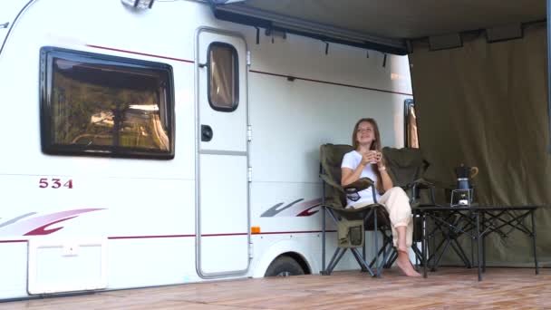 Kobieta siedzi z kubkiem kawy w pobliżu kampera, cieszyć się przyrodą — Wideo stockowe