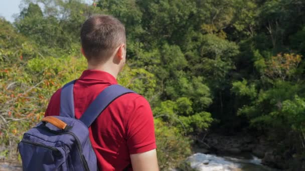 リュック岩の上に立って、川を見て旅行男のバックパックビュー — ストック動画