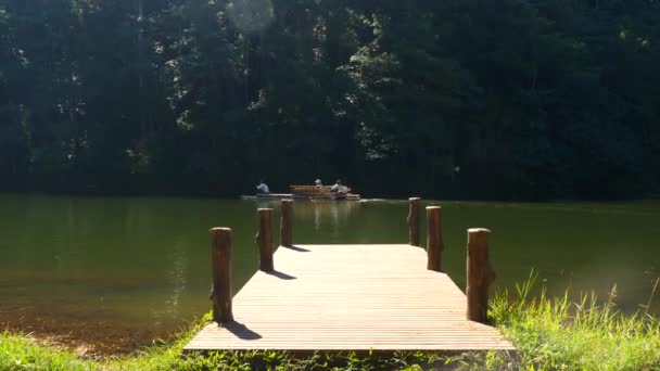 Een houten brug op de rivier met vlot drijvend met mensen op de achtergrond — Stockvideo