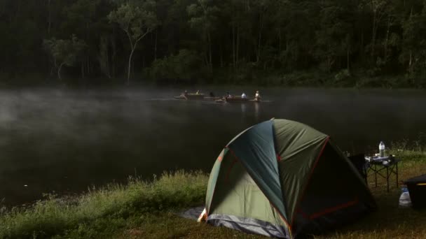 Tent, folding table, and camping gear on fog lake shore in early morning forest — Stock Video
