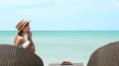 Turkuaz deniz kenarındaki sahildeki kafede oturan genç bir kadın taze meyve yiyor.