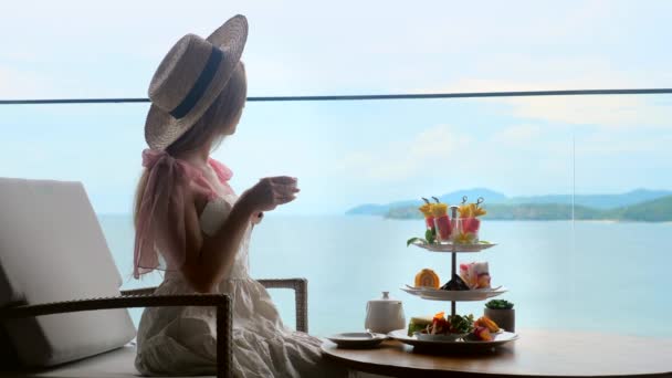 Νεαρή κυρία με λευκό φόρεμα πίνοντας τσάι το απόγευμα τσάι με διάφορα γλυκά — Αρχείο Βίντεο
