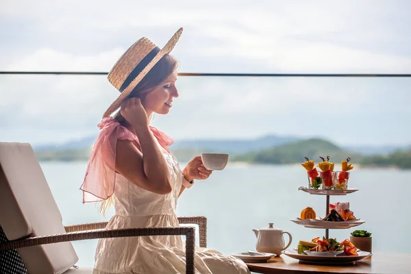 Beyaz elbiseli genç bayan çeşitli tatlılarla ikindi çayı içiyor. — Stok fotoğraf