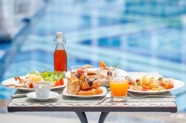 Güzel mavi havuz yolculuğunun yanında nefis yiyeceklerle dolu bir masa.