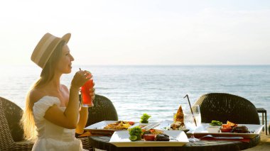 Romantik genç bayan tatilde. Restoranda yemek yer, kokteyl yudumlar.
