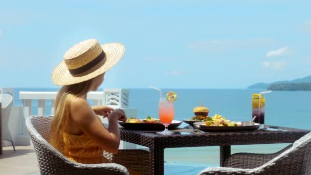 Jeune femme se détendre dans une station tropicale, prendre le petit déjeuner dans un restaurant avec mer — Video