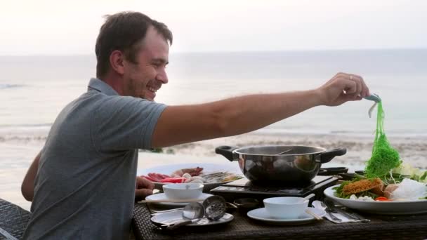 Sukiyaki o Shabu Shabu. Sorridente uomo ispirato cucinare frutti di mare freschi in pentola calda — Video Stock