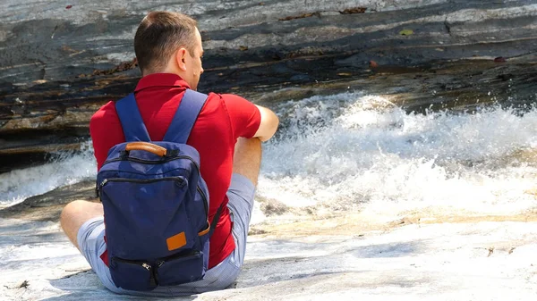 Один мужчина-путешественник с рюкзаком сидит у бурлящей горной реки — стоковое фото