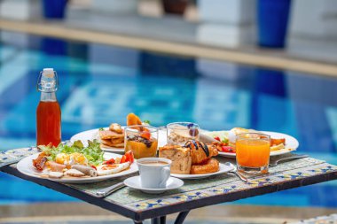 Güzel mavi havuz yolculuğunun yanında nefis yiyeceklerle dolu bir masa.