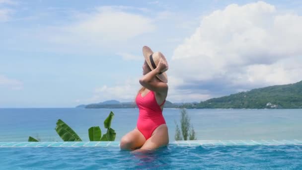 Γυναίκα με κόκκινο μαγιό χαλαρώστε στην πισίνα με θέα στη θάλασσα. Τροπικές διακοπές — Αρχείο Βίντεο