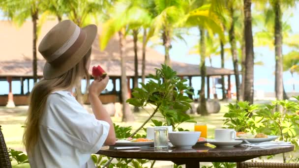 Jonge vrouw eet vers fruit in outdoor hotel restaurant van luxe tropisch resort — Stockvideo