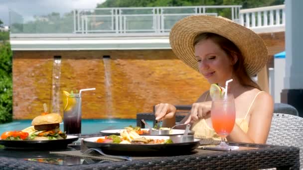 Mujer en sombrero de paja comiendo comida saludable, relajante en restaurante piscina — Vídeo de stock