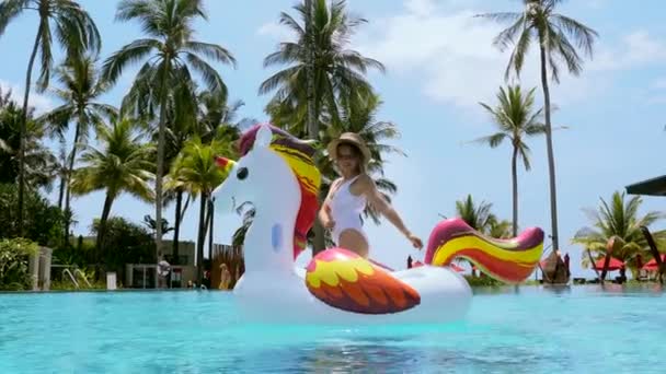 Şişme tek boynuzlu at şiltesindeki tatilci kadın yüzme havuzunda eğleniyor. — Stok video