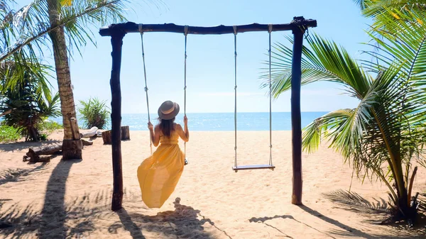 Kobieta turysta huśtawka na huśtawce na piaszczystej plaży z palmami i błękitne morze — Zdjęcie stockowe