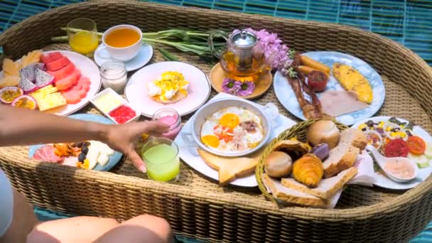 Femme main prendre jus de fruits verre de plateau de petit déjeuner flottant dans la piscine sur la villa — Video