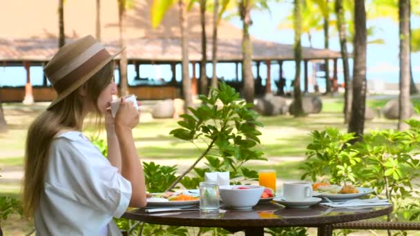 Νεαρή γυναίκα έχουν πρωινό σε πολυτελές ξενοδοχείο με θέα στη θάλασσα στο υπαίθριο εστιατόριο θέρετρο — Αρχείο Βίντεο