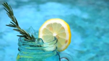 Yüzme havuzunun yanında biberiye ve limon dilimli alkolsüz mavi kokteyl.