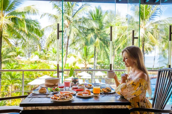 Tropik tatil. Modern otelde kahvaltı yapan kadın, deniz ve palmiye ağaçlarıyla — Stok fotoğraf