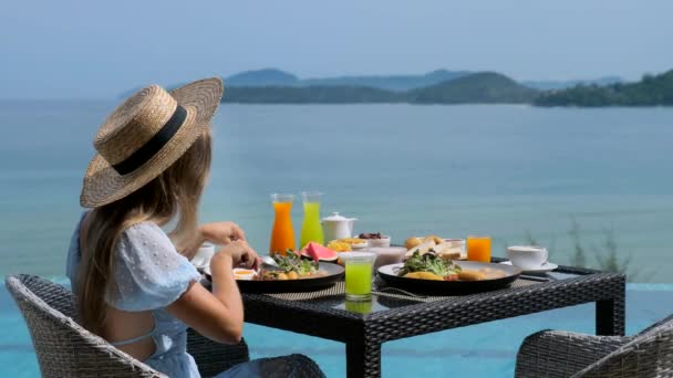 Jovem relaxa em resort tropical, tomando café da manhã em restaurante com mar — Vídeo de Stock