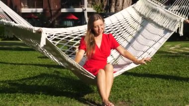 Genç, çekici, gülümseyen kadın modern bir tatil köyünde hamakta oturuyor ve dinleniyor.