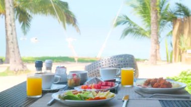 Kumlu sahil, palmiye ağaçları ve salıncaklı tropik sağlıklı kahvaltı.