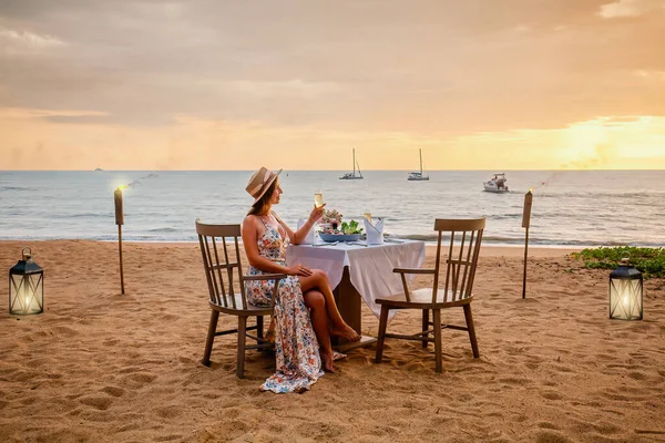 Vrouw zit alleen op tafel met lantaarn voor een romantische maaltijd op het strand — Stockfoto