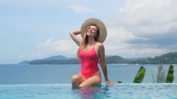Νεαρή αισθησιακή γυναίκα με μαγιό και ψάθινο καπέλο χαλαρώστε στην μπλε πισίνα — Αρχείο Βίντεο
