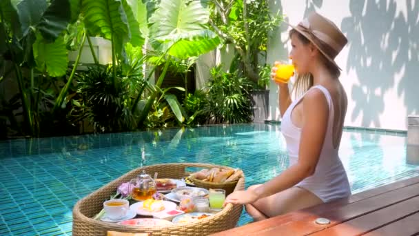 Glückliche Mädchen frühstücken schwimmend im Luxus-Pool im Hotel, trinken Orangensaft — Stockvideo