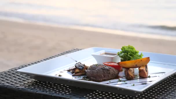 ビーチテーブルの上の白いプレート上のグリル野菜とビーフステーキ,フィレ・ミグノン — ストック動画