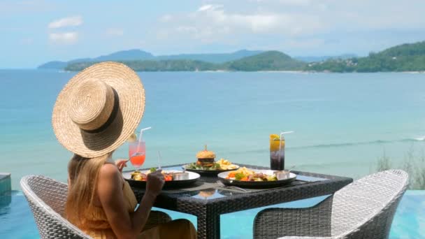 Mulher jantando, sentada no terraço do restaurante perto da piscina com vista azul para o mar — Vídeo de Stock