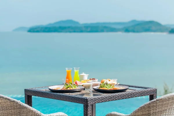 Tropical breakfast with fresh fruit, tea and pastry with ocean and green hills — Stok fotoğraf