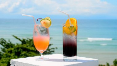 Arka planda deniz plajı olan bar masasında iki taze buzlu moktail.