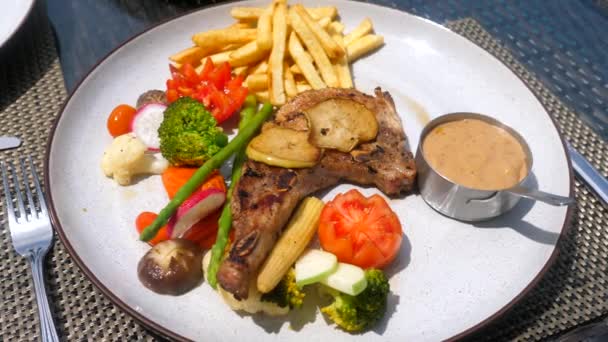 La chuleta de cerdo sirve con verduras, papas fritas y salsa de pimienta — Vídeo de stock