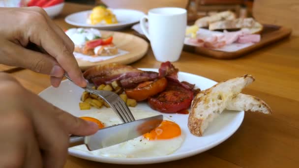 Manos masculinas con tenedor y cuchillo cortado, comer huevos fritos con yema líquida en el desayuno — Vídeos de Stock