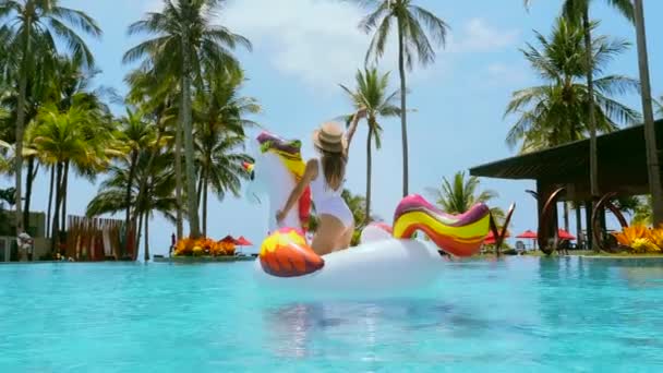 Волнующая молодая женщина танцует и веселится на плавающем единороге в бассейне — стоковое видео